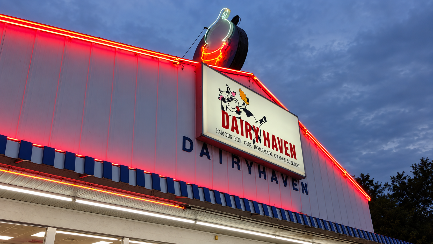 Dairy Haven’s illuminated cow sign, red neon roofline, and blue-striped awning at dusk